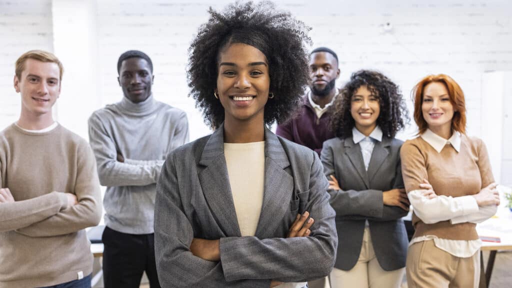 group of young multiracial business people, focus on latin ameri group of young multiracial business people, focus on latin american woman. Smiling young businesswoman stands confidently in front of her diverse team, arms crossed, representing leadership and teamwork.