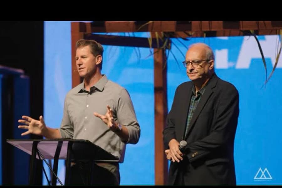 Rev. Daniel Bentley speaking on stage at Maranatha Chapel with Rev. Botrus Mansour beside him.