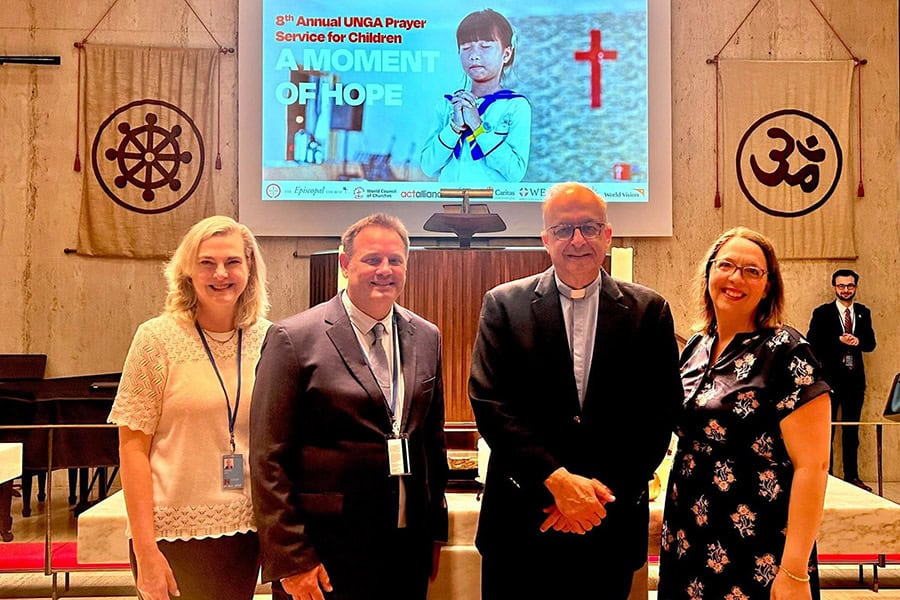 Four people standing together in Tillman Chapel, New York, in front of a screen showing 