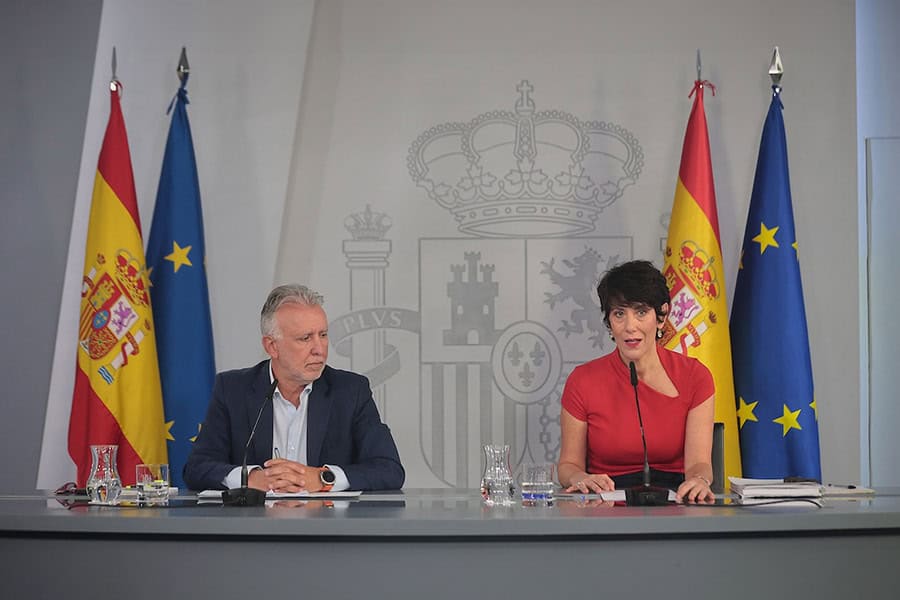 Two Spanish officials at government press conference with national flags